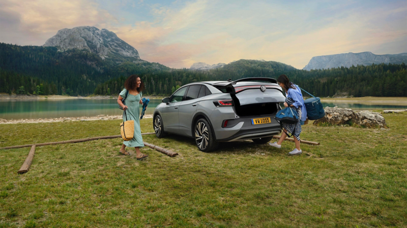 Une ID.5 est garée devant un lac, tandis que deux jeunes femmes remplissent le coffre de valises de camping.