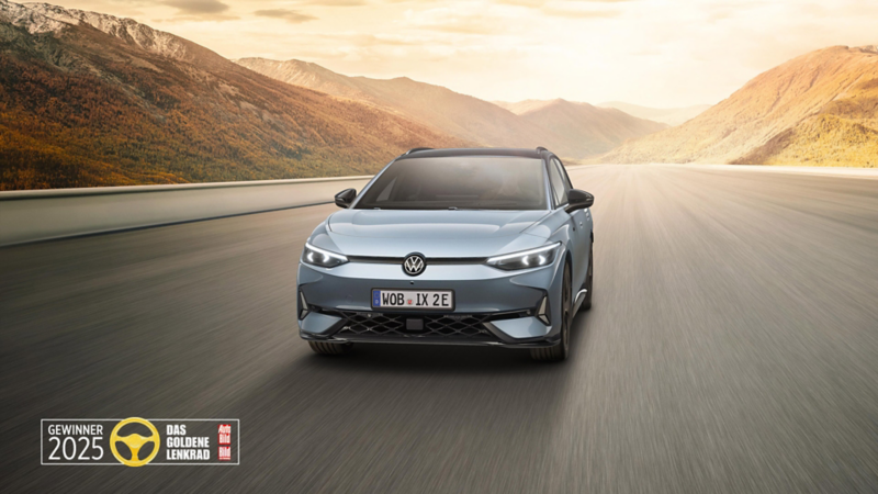 Ein ID.7 GTX Tourer in der Farbe Stonewashed Blue Metallic fährt im Sonnenaufgang auf einer Straße durch die Landschaft. Ebenfalls abgebildet ist das Logo des Goldenen Lenkrads 2025.