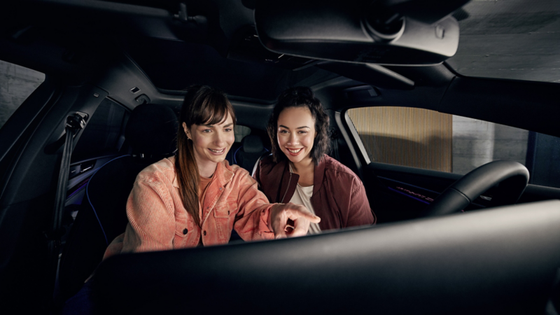Two women sit in the car and use a phone