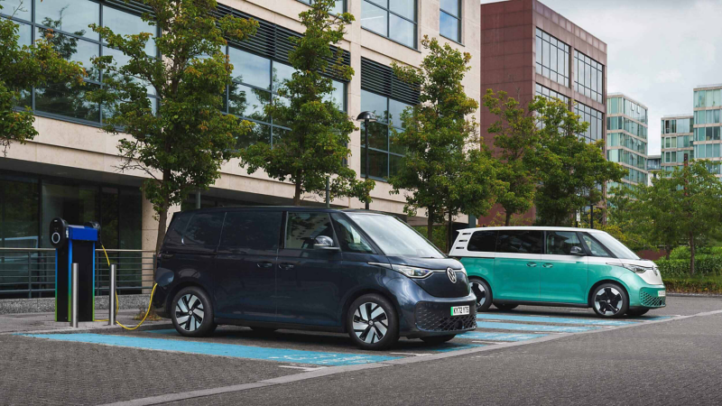 Photo showing two VW ID. Buzz's parked next to each other infront of an office building. 