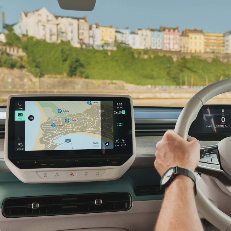 Close up interior photo of a VW vehicle showing a driver using the steering wheel and navigation dashboard module. 