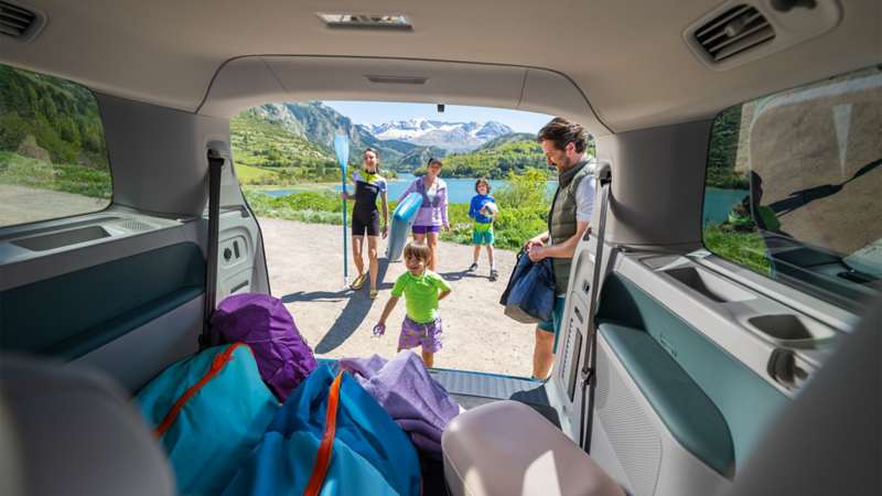 Une famille s'apprêtant à faire une activité au bord d'un lac, vue depuis l'intérieur du coffre ouvert d'un ID.BUZZ
