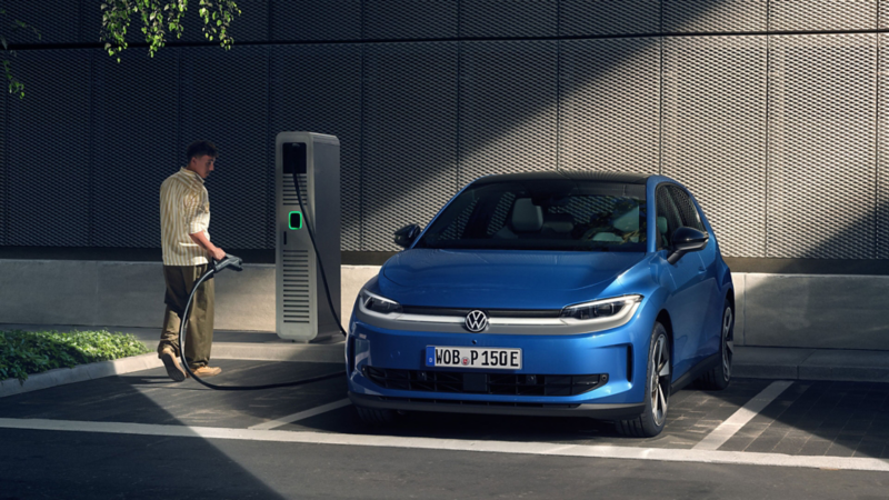 Ein blauer VW ID. Polo Style steht an einer Ladesäule auf einem Parkplatz. Daneben ein Mann mit Ladekabel in der Hand.