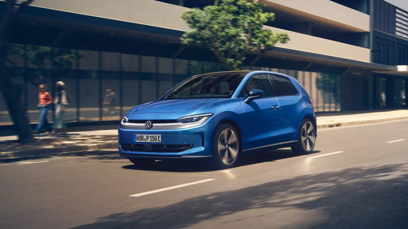 A blue VW ID. Polo is driving through a city with green trees on the roadside.