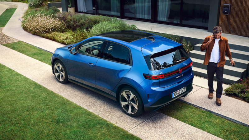 A woman is sitting in the driver's seat of a blue VW ID. Polo and reaches for a bouquet of flowers on the passenger seat.