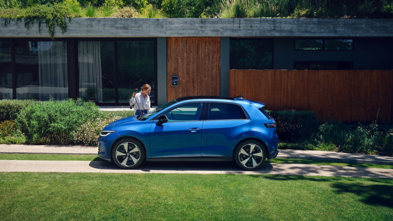Ein blauer ID. Polo steht in der Hofeinfahrt vor einem Einfamilienhaus und wird an der VW Wallbox geladen. 