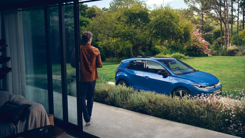 Ein Man schaut von seiner Gartentür aus auf einen blauen VW ID. Polo.