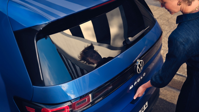 A woman opens the boot of a blue VW ID. Polo.