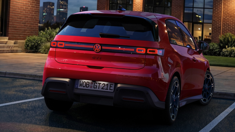 En röd VW ID. Polo GTI sedd bakifrån med upplysta bakljus och logotyp, parkerad framför en kontorsbyggnad.