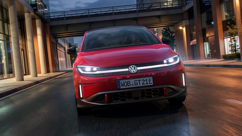 En person kör en röd VW ID. Polo GTI på kvällen genom ett modernt, upplyst affärsdistrikt.