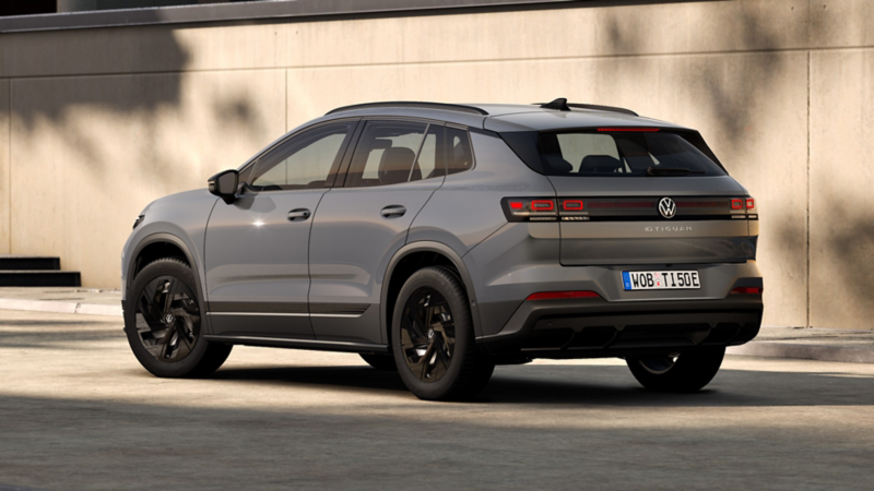 3/4-Heckansicht des ID. Tiguan Trend in grau auf befestigter Fläche vor einer Gebäudewand.