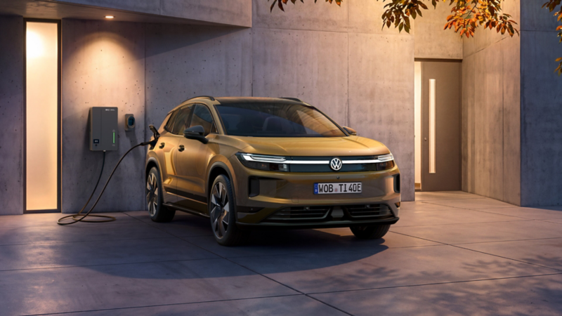 Ein oliv-bronzefarbener VW ID. Tiguan steht vor einem modernen Haus in der Abenddämmerung an einer Elli Bi-Di Wallbox.