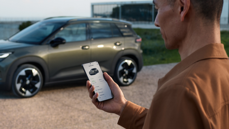 Ein grüner VW ID.Cross parkt an einem Wohnhaus, daneben steht ein Mann und schaut auf sein Smartphone.
