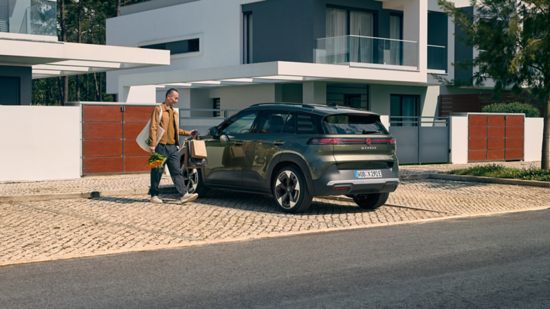 Ein grüner VW ID. Cross parkt an einem Wohnhaus, daneben steht ein Mann und schaut auf sein Smartphone.