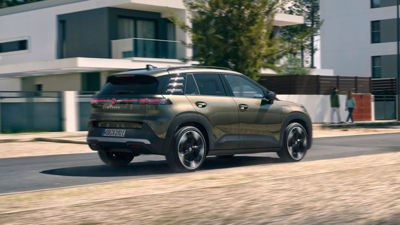 Ein grüner VW ID. Cross fährt durch eine Wohnstraße mit modernen Häusern.