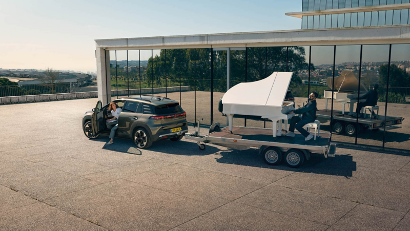 Een Volkswagen ID. Cross trekt een aanhanger met een man achter een vleugelpiano.