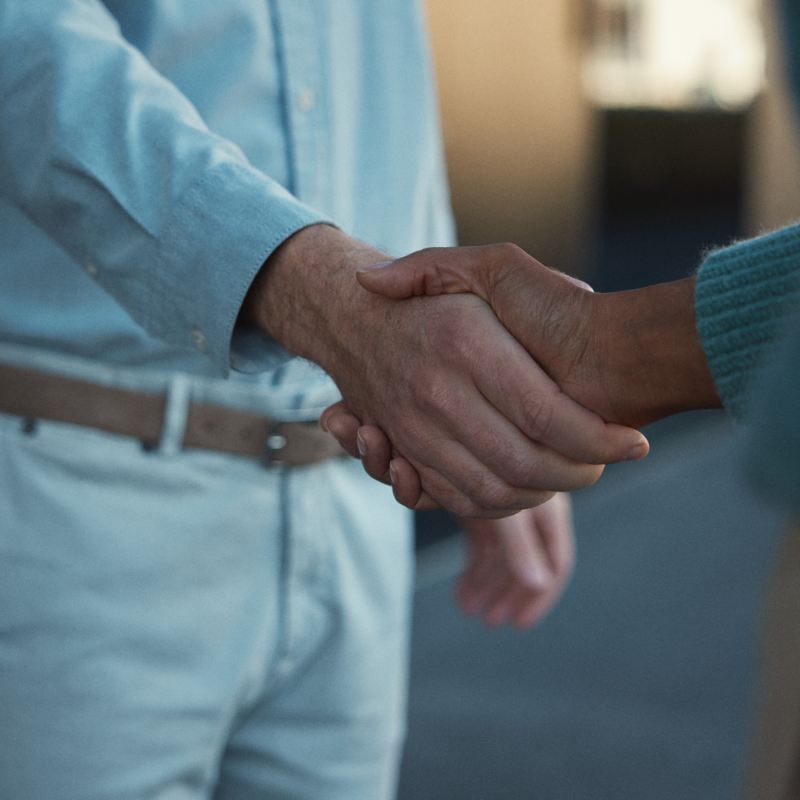 Bildausschnitt zeigt, wie sich ein VW Service Mitarbeiter und eine Geschäftskundin die Hand geben.
