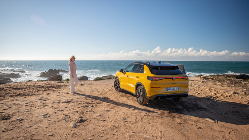 En gul T-Roc står parkerad vid havet, en kvinna står bredvid bilen