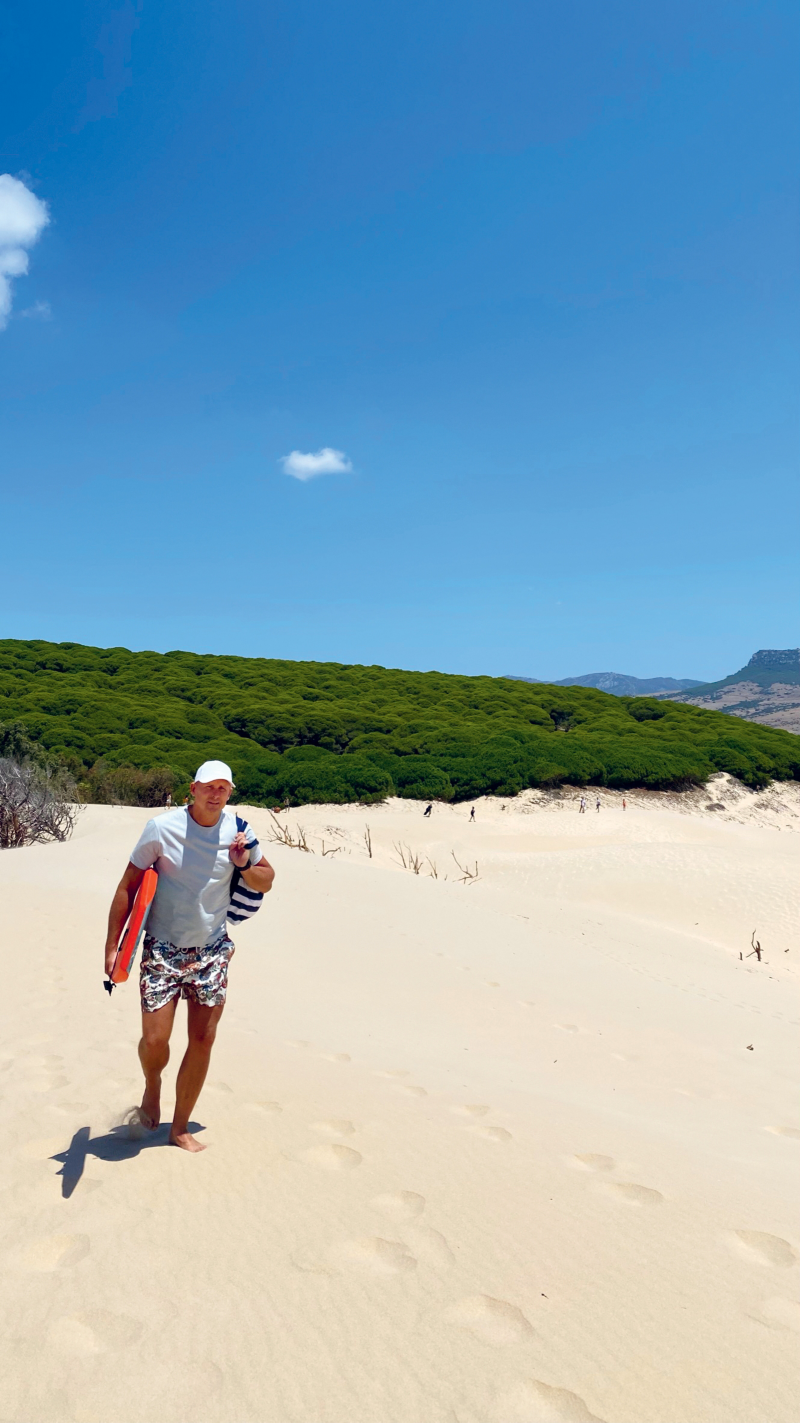 Alexander Dahlin går på en sandstrand med surfbräda under armen