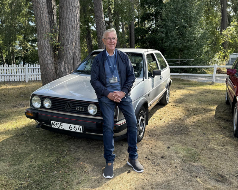 En person sitter på motorhuven på en klassisk Volkswagen Golf GTI som står parkerade på gräs i en parkmiljö.