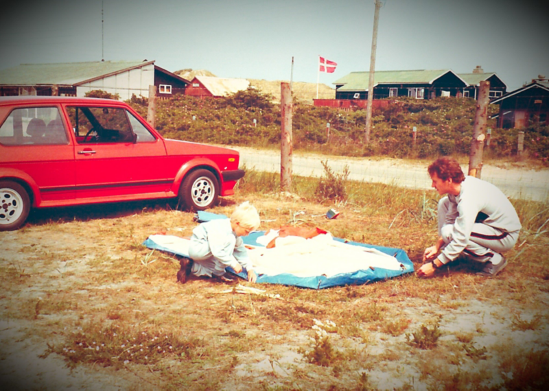 En mand og et barn er ved at sætte telt op ved siden af en rød golf gti