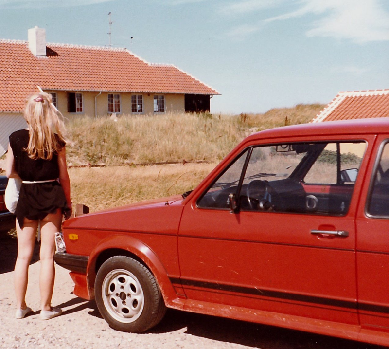En kvinde står ved siden af en rød golf gti ved en strand