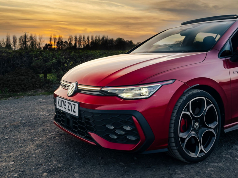 Front three-quarter view of a red Golf GTI on a gravel road at sunset