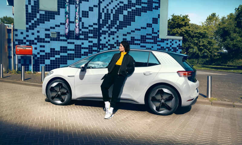 Weißer VW ID.3 mit optionalen Felgen Sanya, Blick auf die Seite, Frau lehnt an Auto.