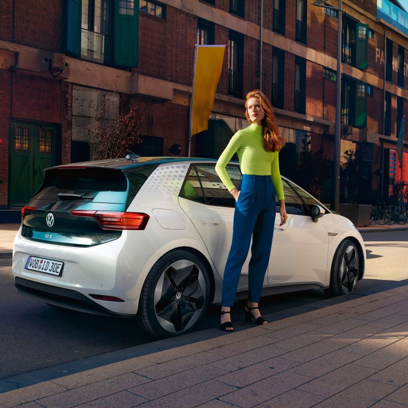 Frau steht vor weißem VW ID.3, der am Straßenrand parkt.