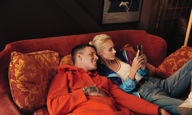 A couple is lounging on a couch looking at a smartphone; thanks to the SIM card installed in the ID.4, the car is online when required.
