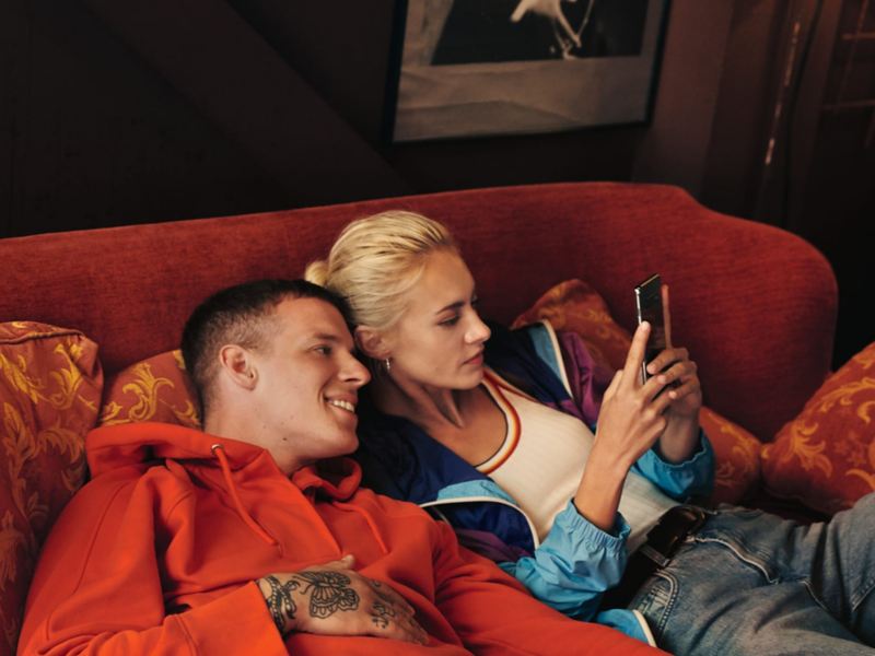Hombre y mujer tumbados cómodamente en un sofá, miran un móvil