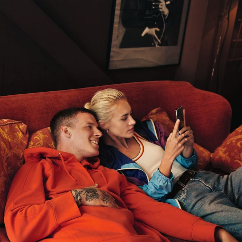 Uomo e donna sono comodamente seduti su un divano e guardano lo smartphone