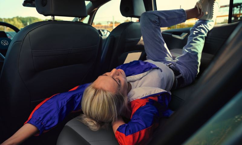 Jauna moteris atsipalaidavusi sėdi ant galinės VW ID.3 sėdynės