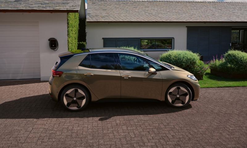 Une VW ID.3 est garée devant une maison avec garage et est raccordée à une wallbox par un câble de recharge.