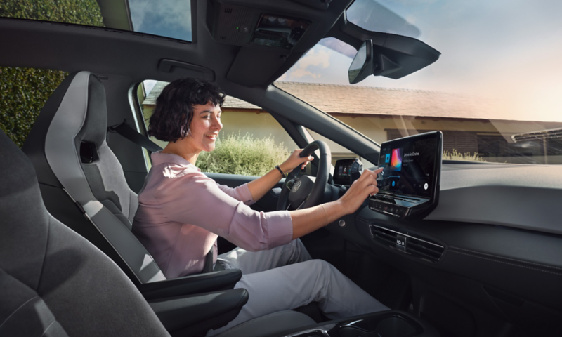 Femme assise place conducteur dans une Volkswagen ID.3 qui interagit avec le système d'infodivertissement