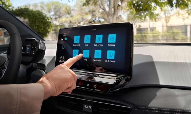 Eine Hand bedient das Display auf der Mittelkonsole im VW ID.3. Auf dem Touchscreen sind diverse Icons zum Anklicken sichtbar.
