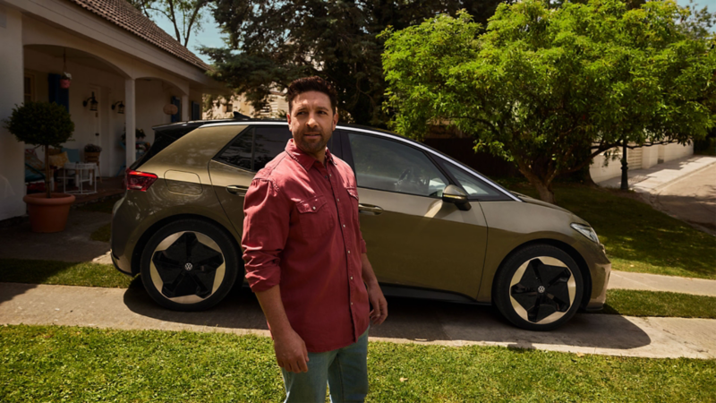 Un homme en chemise rouge se tient devant une ID.3 garée devant une maison individuelle.