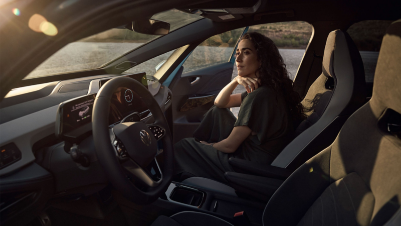 Une femme est assise sur le siège passager et regarde au loin, l'air rêveur, à travers le pare-brise.