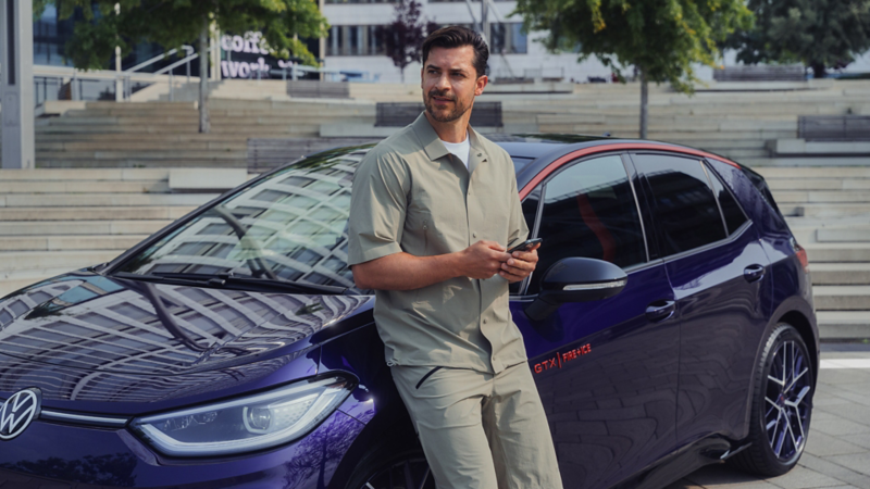 Un jeune homme est assis sur le côté conducteur du capot d'une VW ID.3 GTX FIRE+ICE violette.
