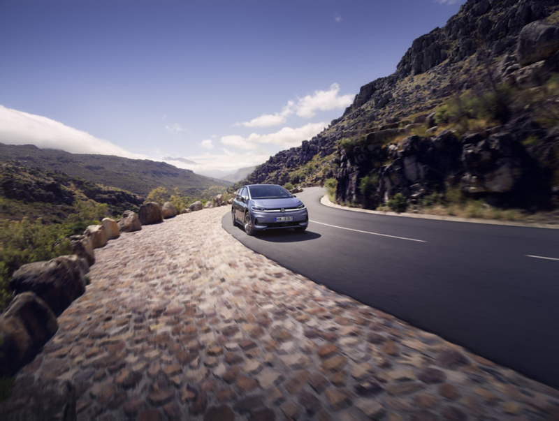 A blue VW ID.3 Neo is driving on a winding mountain road. 
