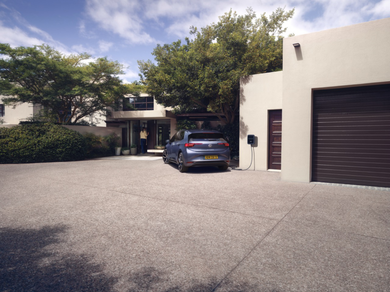 A blue VW ID.3 Neo is charging at a wall box in front of a detached family house. 