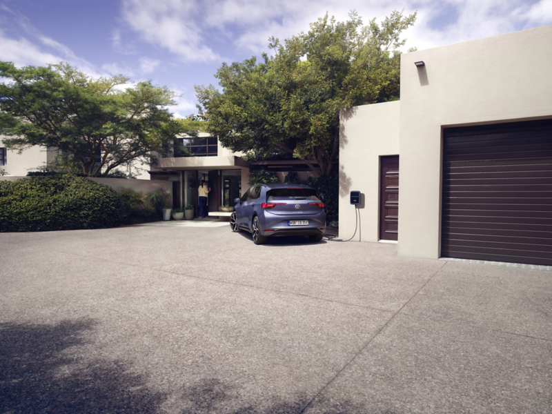 A blue VW ID.3 Neo is charging at a wall box in front of a detached family house. 