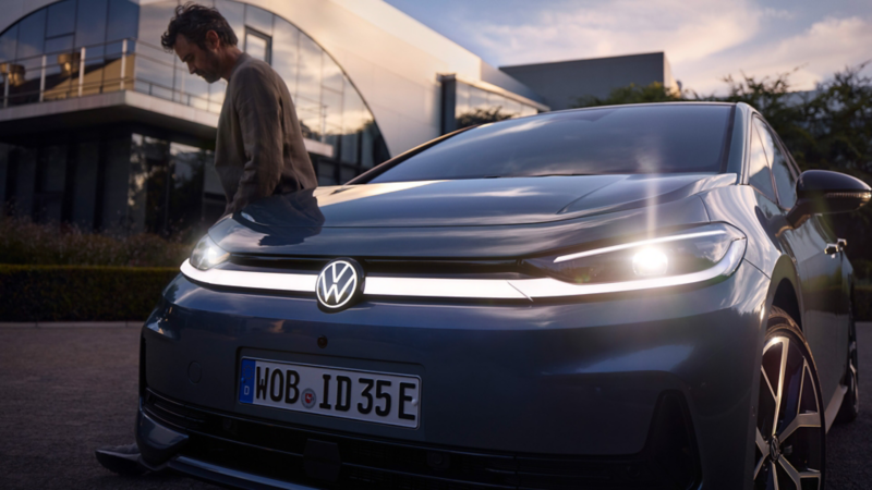 Lichtsignatur mit beleuchtetem VW-Logo an der Front eines blauen VW ID.3 Neo, ein Mann lehnt am Fahrzeug.