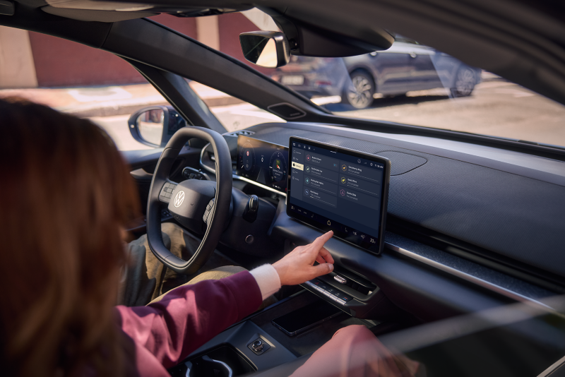 Eine Frau sitzt in einem Volkswagen und bedient die Mein Fahrstil App.