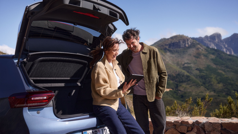 Eine Frau sitzt in einem geöffnetem Kofferraum eines VW ID.3 Neo mit einem Tablet in der Hand.