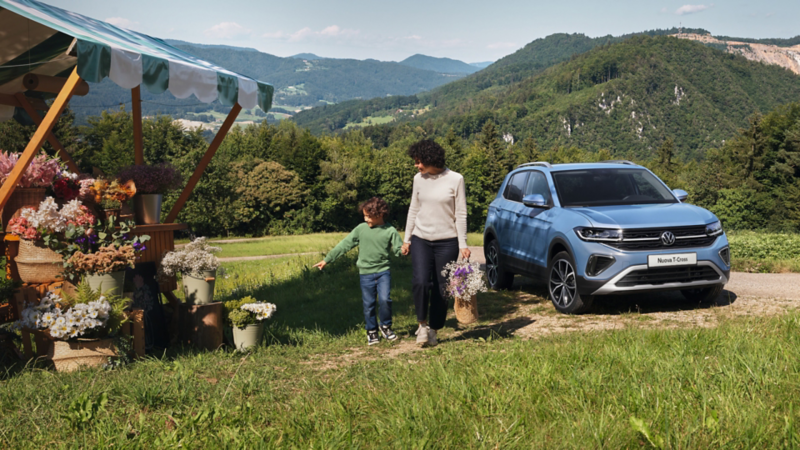 T-Cross parcheggiata in un contesto montuoso con prati attorno. Una mamma e suo figlio passano di fronte ad un chiosco che vende fiori