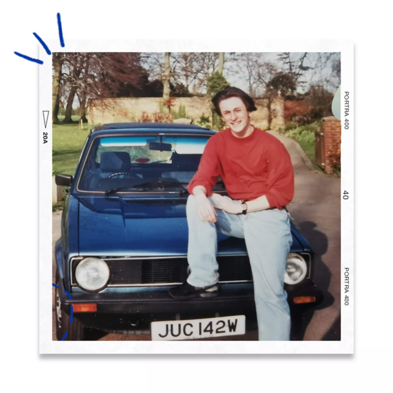 Person sitting on the bonnet of a blue Volkswagen Golf Mk1 parked on a residential driveway