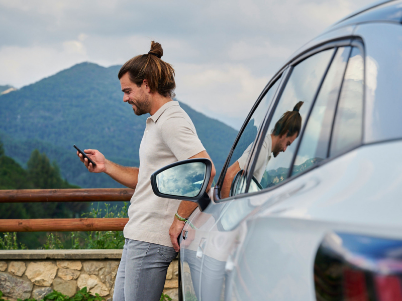 Mężczyzna ze smartfonem opiera się o Volkswagena ID. W tle góry.