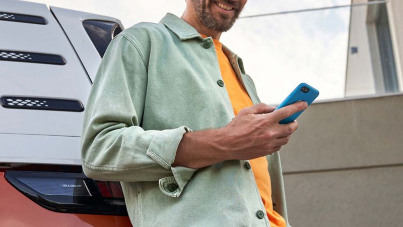 A man leaning against the rear of an ID. Buzz while looking at his phone. 