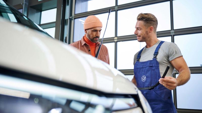 A VW technician talking to a customer while standing next to a vehicle. 